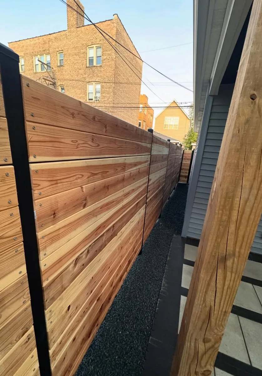 Horizontal cedar fence boards mounted on black steel posts along a side yard, with a black gravel bed and paver walkway beside it