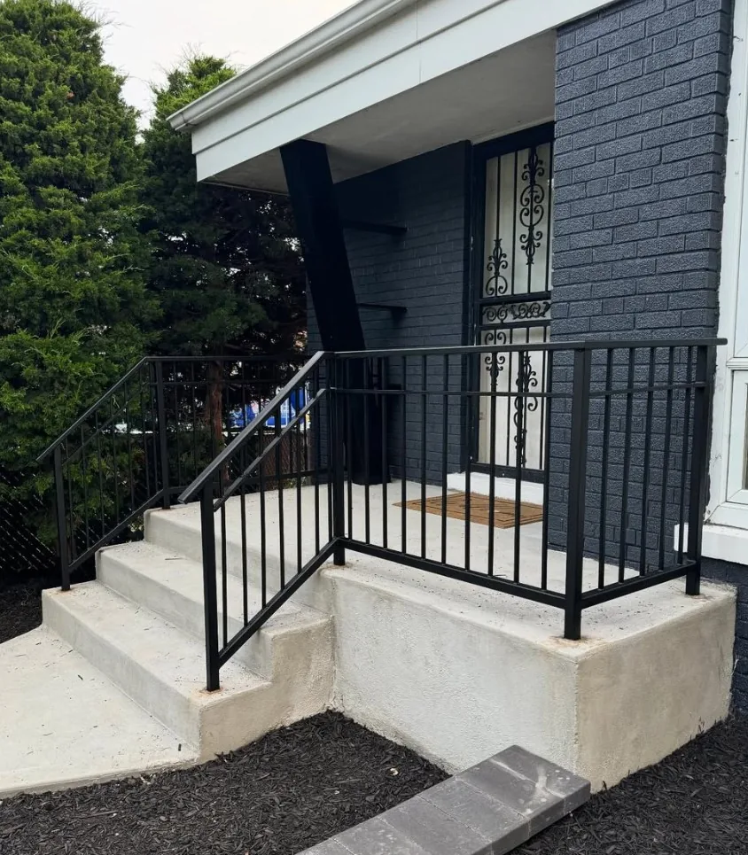 Black steel porch railing and matching stair railing on a poured concrete stoop and steps at a painted brick house